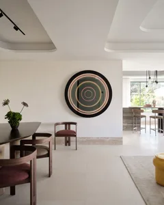 Modern dining room with a circular wall decoration, wooden table and chairs, and a large window.