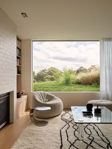 Modern living room featuring a glass table, white rug, and comfortable seating with a view of the greenery outside.