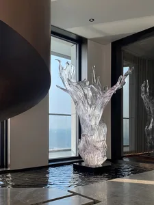 A transparent glass sculpture resembling water spilling out of a vase, placed in a modern lobby with a water feature and larg