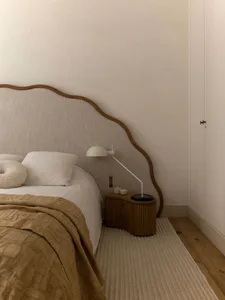 Minimalist bedroom with a textile comforter, wooden headboard, and metallic bedside lamp.