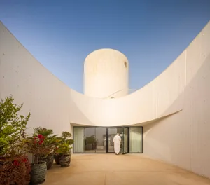 A modern, minimalist concrete house with curved walls and a circular tower.