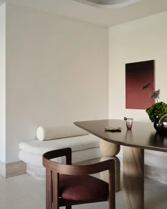 Modern minimalist dining room featuring a wooden table and chairs, with a white bench and abstract red artwork.