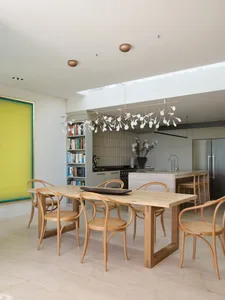 Modern minimalist kitchen featuring wooden elements with a bookshelf, pendant lighting, and a view into the open-plan living 