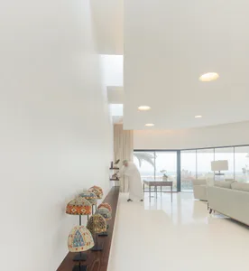 Spacious, minimalist living room featuring concrete flooring and walls, with large windows overlooking the ocean.
