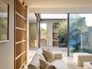 A modern minimalist residential interior featuring a white couch, wooden accents, and a large glass window.