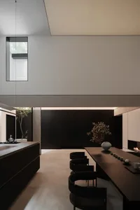 Modern minimalist kitchen with sleek black appliances and wooden dining table surrounded by black chairs.