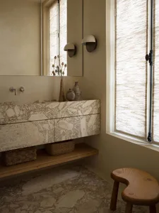 Modern, minimalist bathroom featuring a floating marble vanity, decorative vases, and woven window blinds.
