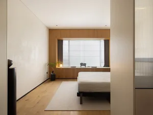 A minimalist bedroom with wood accents, a bed in the center, and a large window with curtains.