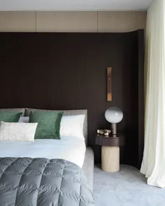 Minimalist bedroom with a bed, green pillows, and a modern lamp on a wooden nightstand.