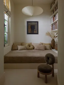 A minimalist bedroom featuring a textile sofa with round cushions, a hanging light fixture, and a bookshelf filled with books