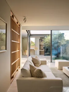 Modern minimalist living room with white sofa, floor lamp, and olive tree in the background.
