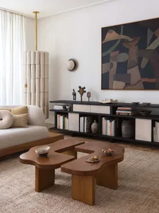 A modern minimalist living room featuring a white fabric sofa, abstract artwork, and organic-shaped wooden coffee tables.