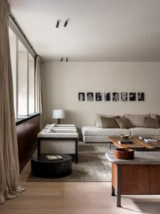 A minimalist living room with neutral-toned furniture and decor, featuring floor-to-ceiling windows and a modern sofa.