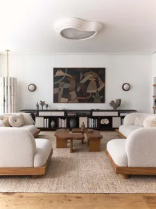 A minimalistic living room with beige wool sofas and wooden accents, featuring abstract art and a low-profile coffee table on