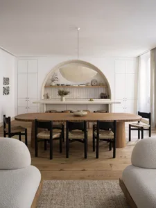 A modern, open-plan living and dining room with minimalist decor, wooden furnishings, and a marble counter.