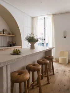 A modern residential kitchen featuring minimalist design with wooden stools and countertops.