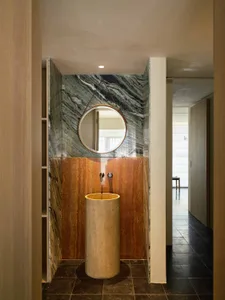 Modern bathroom interior with a cylindrical pedestal sink, marble walls, and circular mirror.