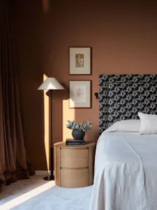 A modern bedroom with a patterned upholstered headboard and a white bedspread. The room features a side table with a vase of