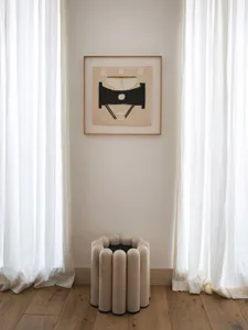 A modern room setting with white curtains and a white side table with a black base.