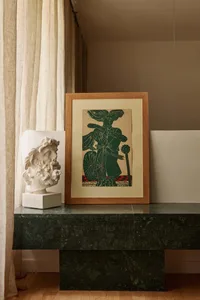 A framed artwork and a marble bust displayed on a green marble console table.