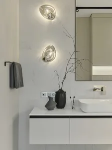 A minimalist bathroom featuring marble finishes, wall lights, a white floating vanity, and a vase with branches.