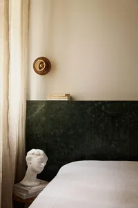 A minimalist bedroom featuring marble walls, a linen curtain, and a wooden bed frame.