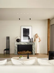 A minimalist living room with a marble fireplace, black furniture, and contemporary decor.