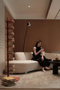 A modern living room featuring a sleek, curved sofa, a tall bookshelf, and a minimalist floor lamp.