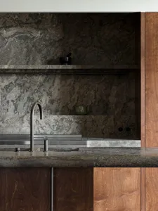 A modern kitchen interior featuring a granite countertop and backsplash, with a metal faucet and wooden cabinets.
