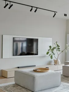 A modern living room featuring a light wood floor, minimalist furniture, and a sleek flat-screen TV mounted on the wall.
