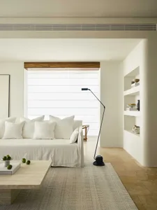 Modern living room featuring a white couch with multiple pillows and a black floor lamp on a beige rug in front of a window w