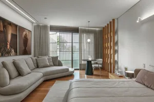 A modern minimalist bedroom featuring a fabric sectional sofa, white bed, and wooden flooring.