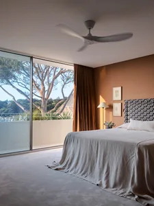 A modern minimalist bedroom featuring linen bedding, wooden headboard, and glass window with a view of outdoor greenery.