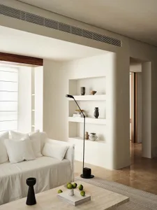 A minimalist living room featuring neutral-toned walls, a white sofa, and a coffee table with green apples.