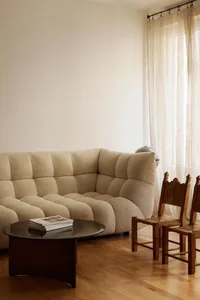 A minimalist living room featuring a beige upholstered sofa, a dark wooden coffee table with a glass top, and two wooden side