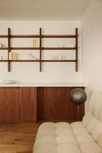 A modern minimalist living room featuring a wooden cabinet, white sofa, and sleek shelving unit.