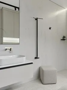 A minimalist bathroom with white marble tiles, a floating vanity, and a wall-mounted sink and faucet.
