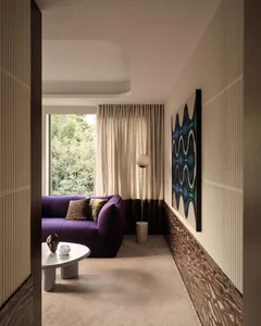 A modern living room featuring textured curtains and concrete flooring, with a purple sofa, white coffee table, and a lamp.