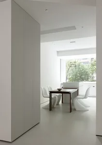 A minimalist kitchen with white cabinets and wood accents, featuring a modern dining table and chairs.
