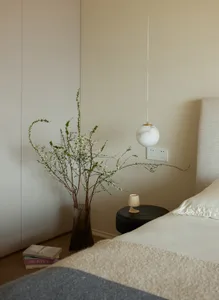 A modern bedroom featuring a bed with a beige cover and a black circular side table with a small white cup on it.