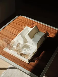 A modern house model made of plastic, featuring a unique architectural design with a central courtyard, surrounded by trees a