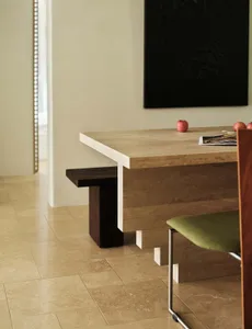 A modern interior space featuring a concrete table with a dark wooden bench and a green upholstered chair.