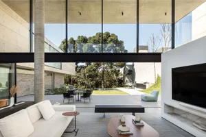 A modern living room featuring white concrete walls and large glass windows.