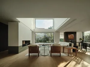 A modern living room with large windows, white walls, wooden flooring, a fireplace, and a white sofa with cushions.