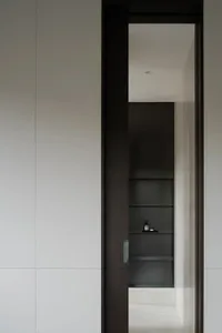 這張圖片呈現一扇帶有金屬框的簡約門，通往一間擁有白牆與白地板的房間。