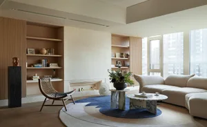 A modern minimalist living room with wooden shelves, marble coffee tables, and a wool rug.