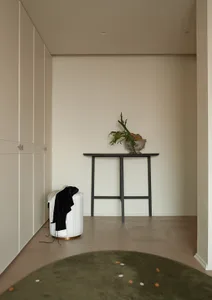 A minimalist entryway with neutral-toned walls, a wooden table, and a green rug with small white dots.