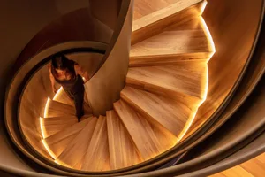 Person walking up a spiraling wooden staircase illuminated by LED lights at night.