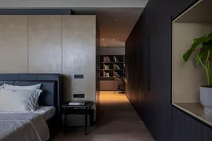 A modern, minimalist bedroom featuring dark wooden furniture and a luxurious bed setup with a black headboard and white beddi