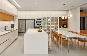 Modern, minimalist residential kitchen featuring a large white marble island, wooden dining table, and glass display shelves.